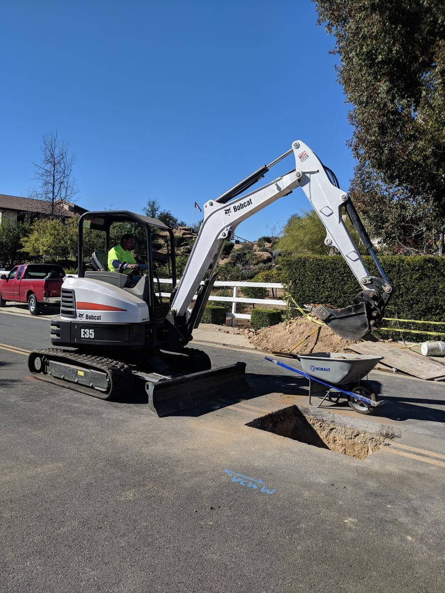 Compact excavator positioned in a street for a BBC Rooter underground sewer repair