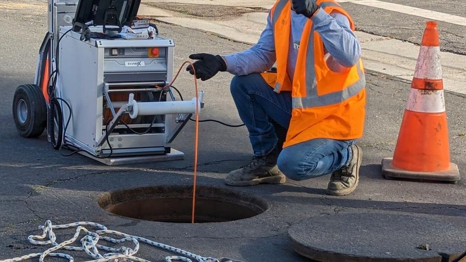 BBC Rooter technician running a CCTV sewer camera at an open manhole in a Valley street
