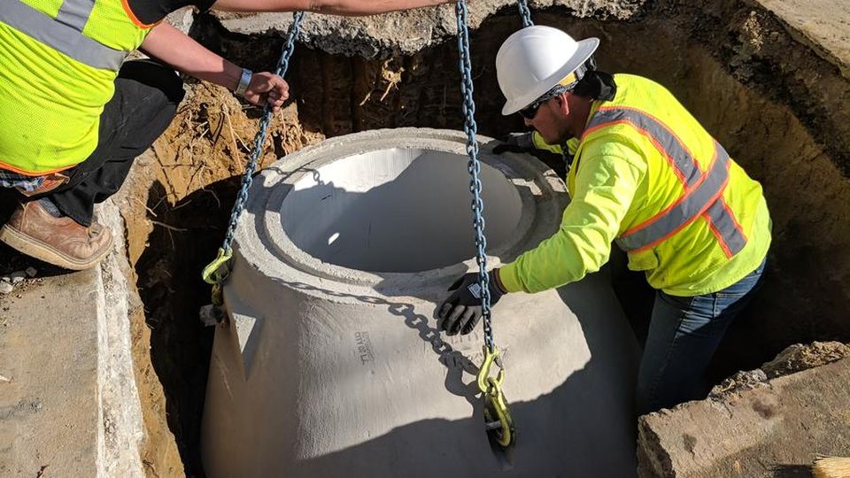 BBC Rooter crew in hard hats and vests setting a precast concrete manhole section